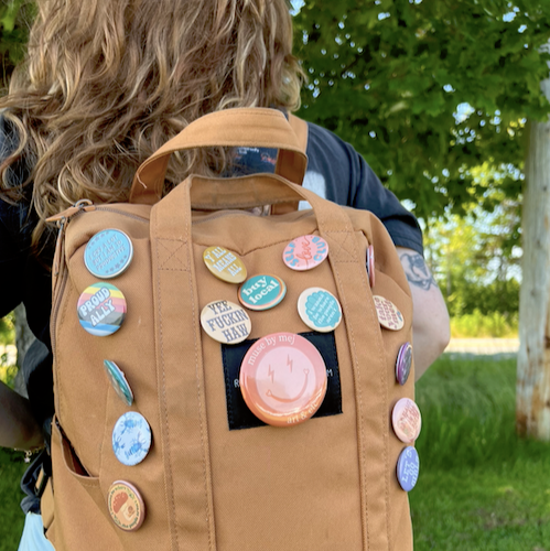 Person wearing a brown backpack with colorful buttons outdoors